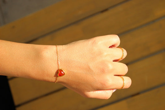 Delicate gold bracelet with a small red heart charm