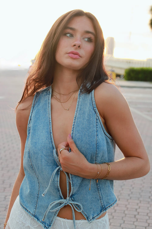 A woman wearing a light blue denim halter crop top with front tie details, photographed outdoors on a paved walkway.