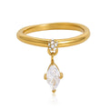 A gold ring with a polished band, a small cluster of clear stones at the top, and a dangling marquise-cut clear gemstone, shown on a white background.