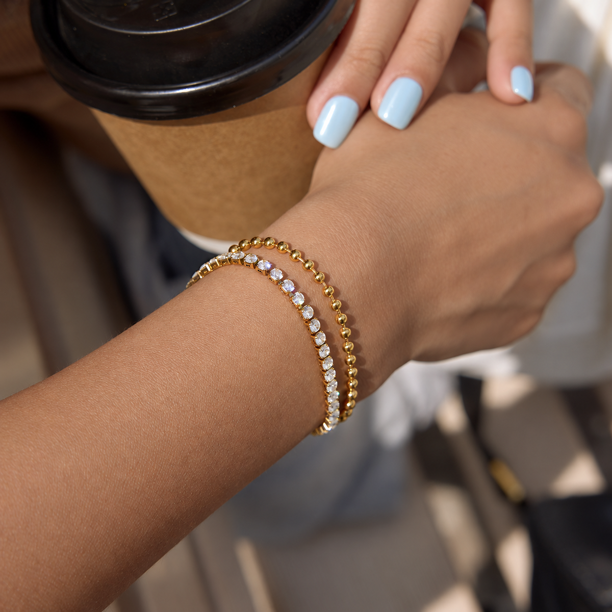 Hand holding a coffee cup with a gold bracelet on a blurred background