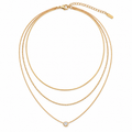 A gold multi-layer necklace featuring three distinct chain styles: a thin snake chain, a beaded chain, and a delicate chain with a single bezel-set clear gemstone pendant, displayed on a clean white background.