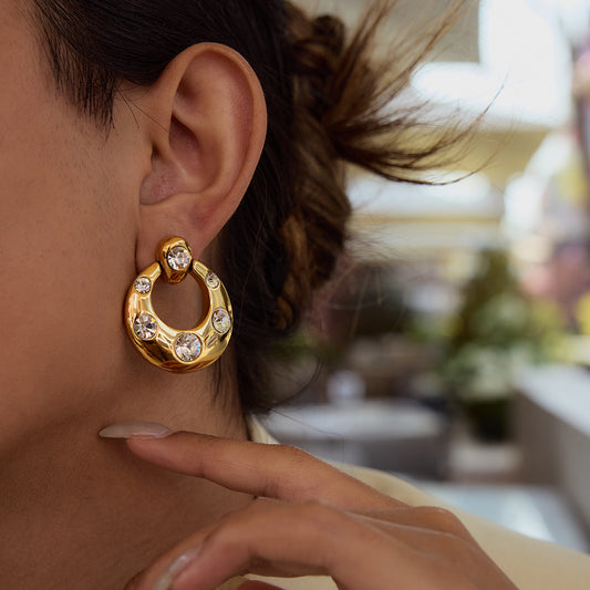 Chunky gold open circle earrings with scattered bezel-set cubic zirconia stones and CZ stud top on white background