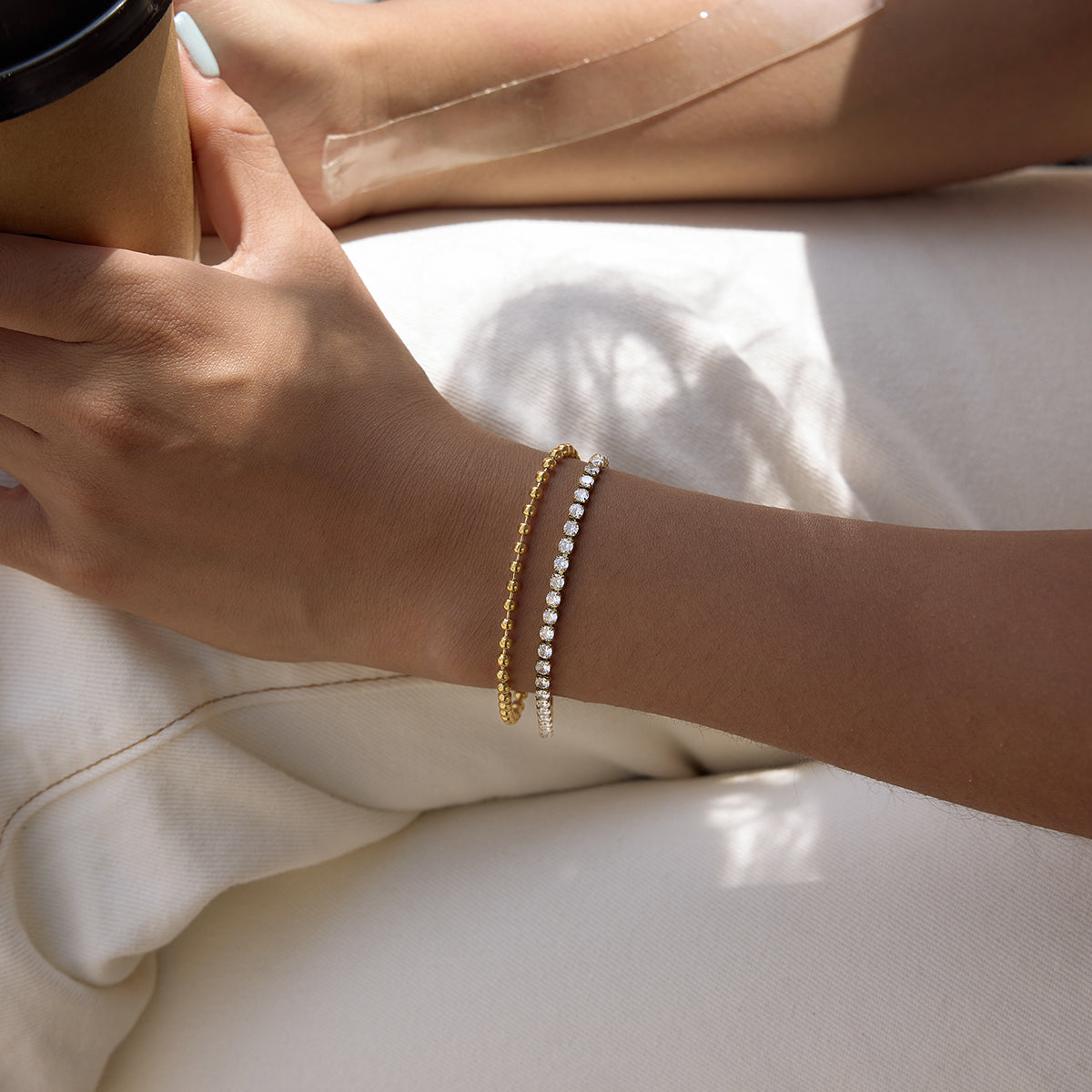 Close-up of a hand wearing two gold bracelets on a light background