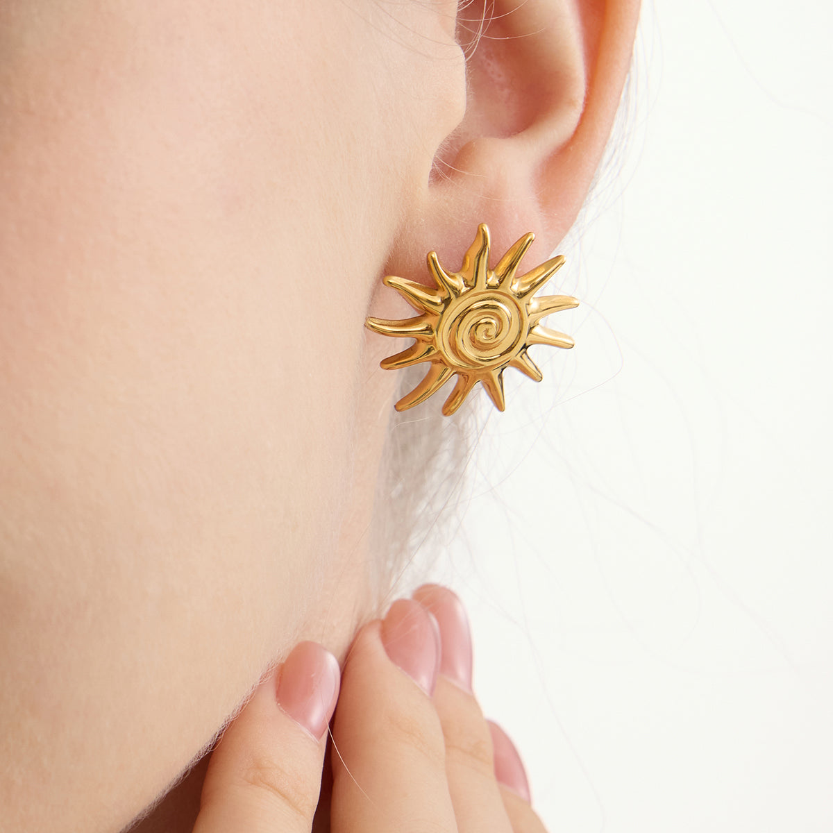 Oversized gold sunburst stud earrings with spiked rays and spiral center on white background