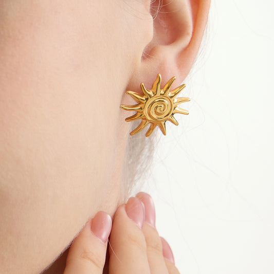 Oversized gold sunburst stud earrings with spiked rays and spiral center on white background